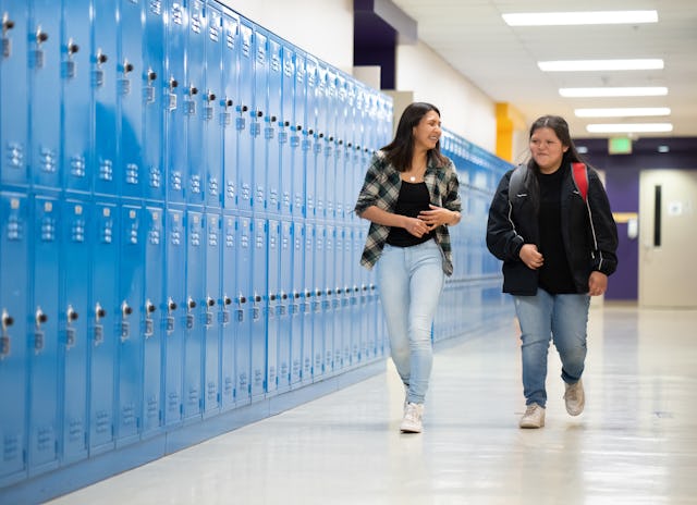 Two girls walk down the hall together in high school.