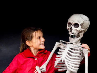 A girl holds a fake human skeleton and laughs.