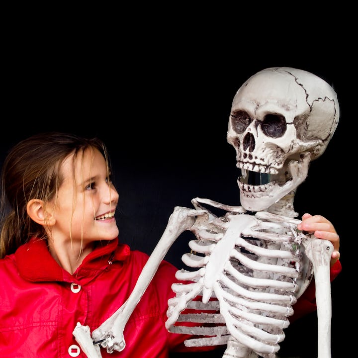 A girl holds a fake human skeleton and laughs.