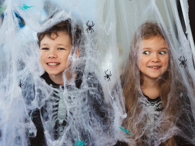 Two kids in fake spider webs laugh.