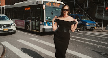The comedian Catherine Cohen standing on a New York City crosswalk in a form-fitting black dress.