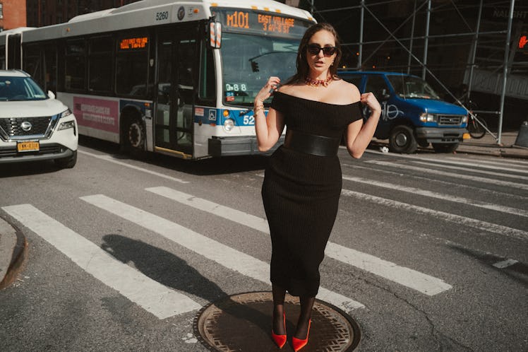 The comedian Catherine Cohen standing on a New York City crosswalk in a form-fitting black dress.