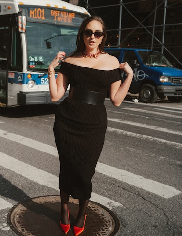 The comedian Catherine Cohen standing on a New York City crosswalk in a form-fitting black dress.