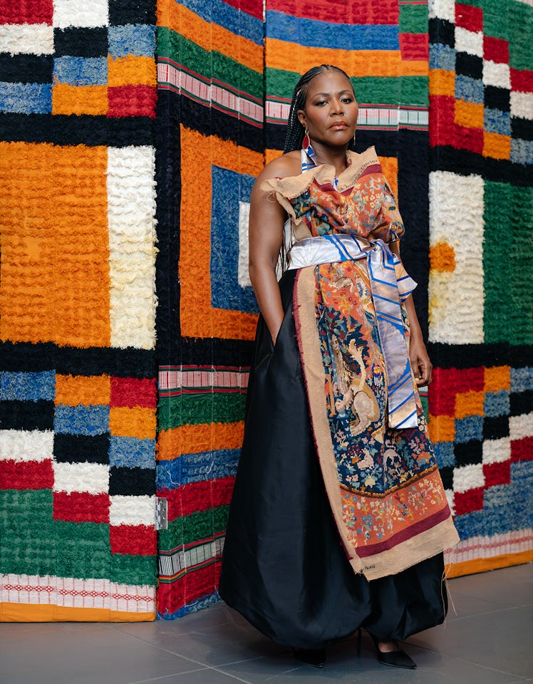 Reni Folawiyo wears a colorful dress, earrings and black shoes.