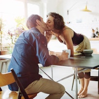 Man and woman kissing at the breakfast table.