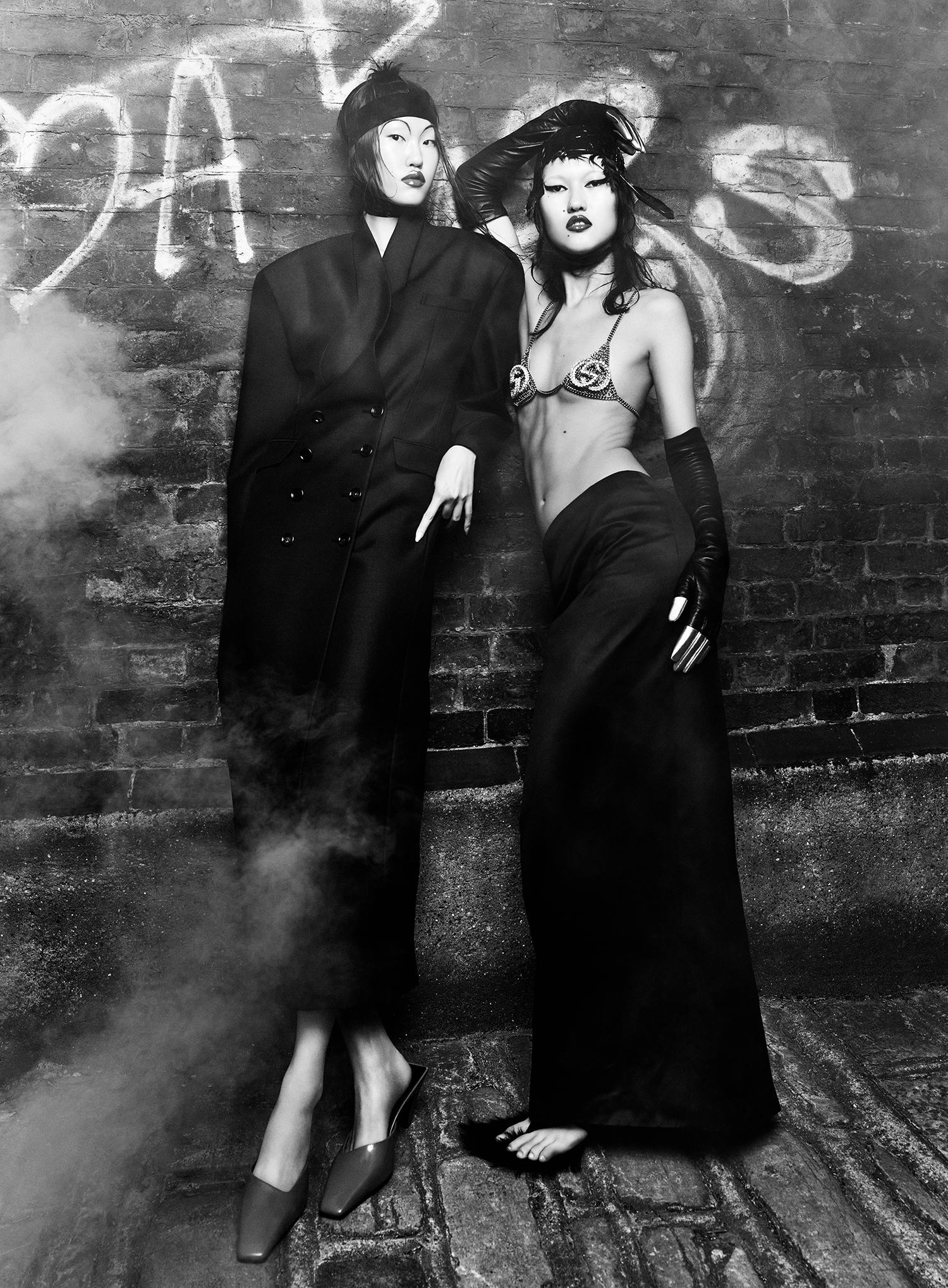 Kim wears a black coat and shoes. Toktorova wears a bra, skirt, gloves, and shoes.