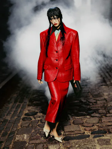 Jia wears a red leather blazer, red leather skirt, black clutch bag, and beige shoes.