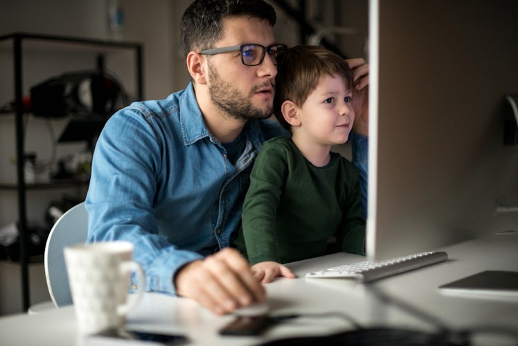 A dad with his son on his lap works from home at a desktop.