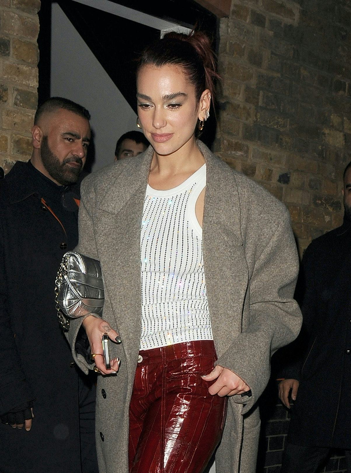 Dua Lipa wears a white tank, burgundy pants, white pumps, and the latest Gucci Horsebit Chain bag.