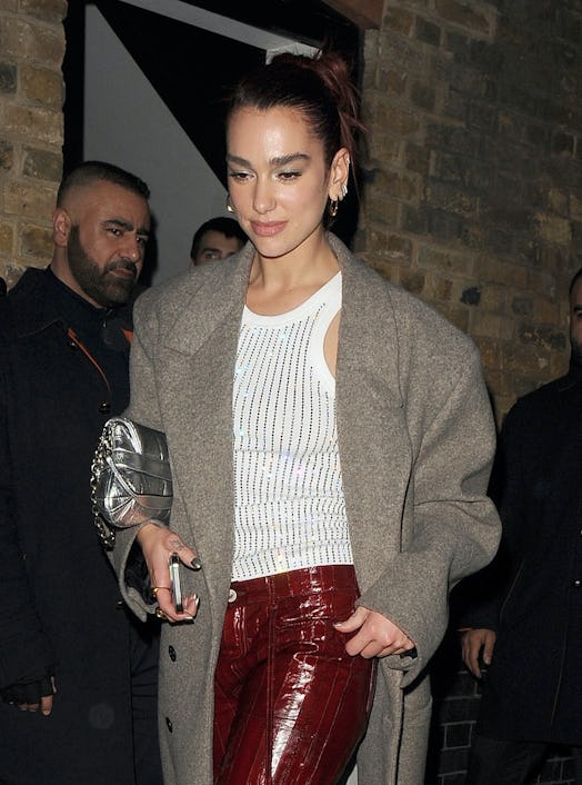 Dua Lipa wears a white tank, burgundy pants, white pumps, and the latest Gucci Horsebit Chain bag.