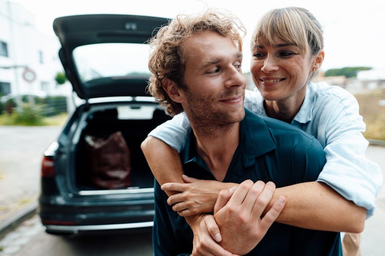 Woman hugging man from behind as they stand near an open hatchback trunk