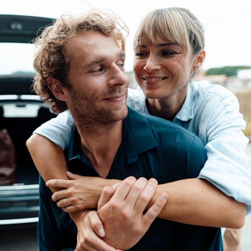 Woman hugging man from behind as they stand near an open hatchback trunk