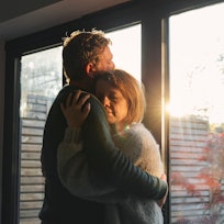 Man hugging woman by an open window as the sun streams in