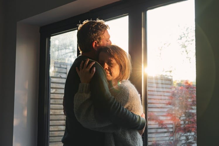 Man hugging woman by an open window as the sun streams in