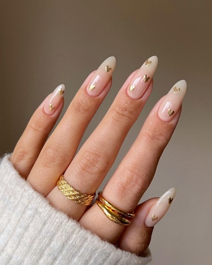 Neutral nails with tiny gold heart nail art are an on-trend Thanksgiving 2023 nail design.