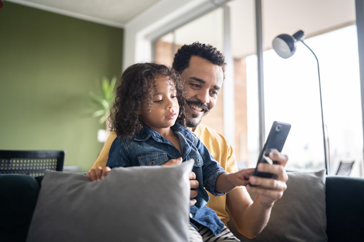 A dad sitting on a couch with his child in his lap, using a cell phone.