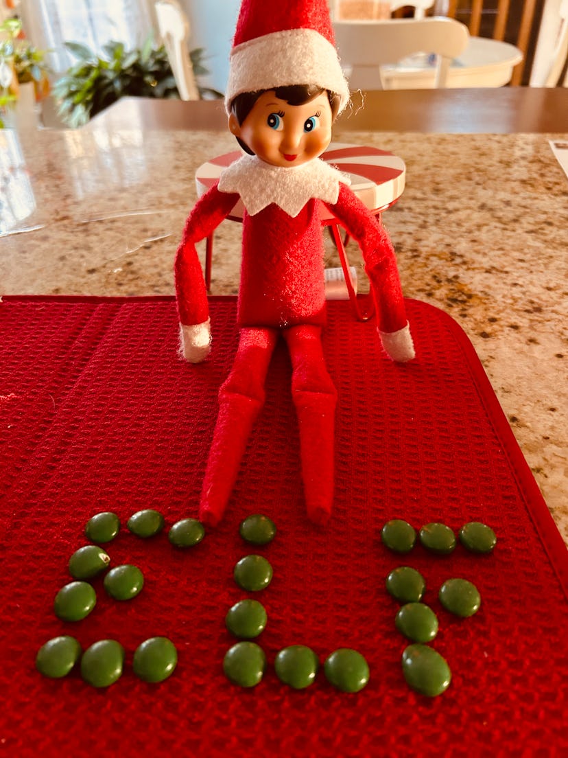 elf on the shelf sitting next to m&ms that spell out "ELF"