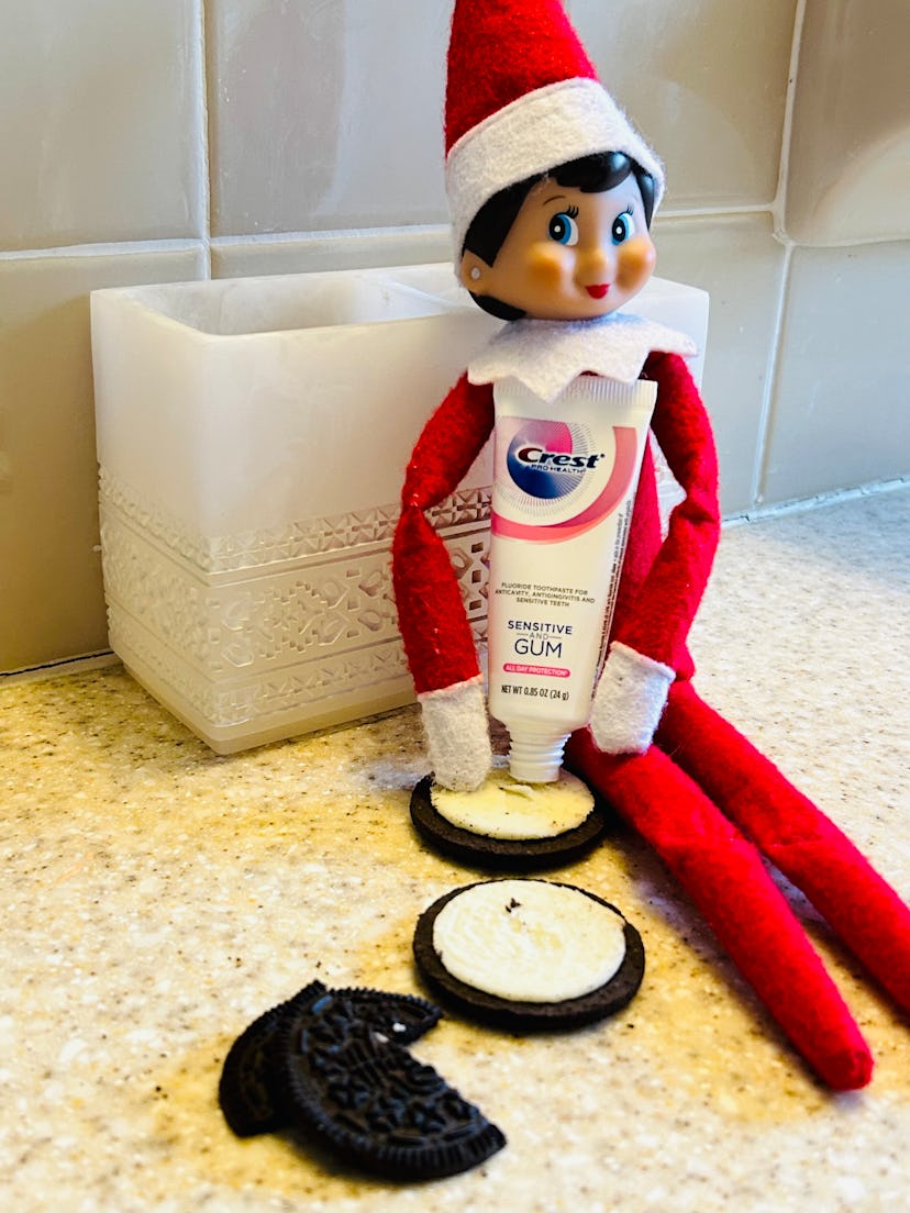 elf on the shelf "replacing" the cream of an Oreo with toothpaste, holding a toothpaste tube over th...