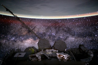 photo of the edge of Earth's curvature, haloed by a faint but distinct glow, with a dense starfield ...
