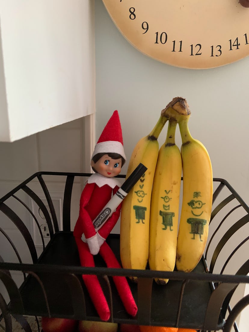 elf on the shelf holding a marker sitting next to bananas with minion drawings on them so it looks l...