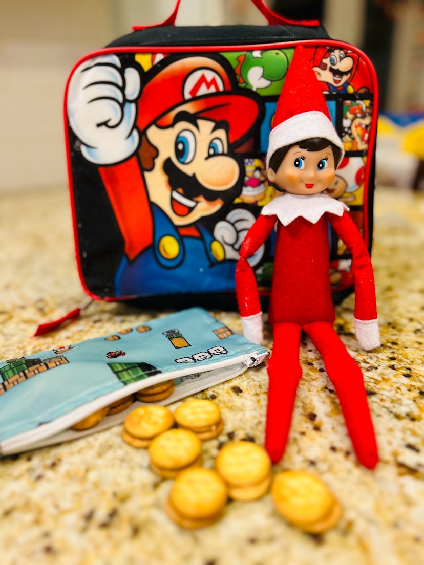 elf on the shelf next to a lunchbox and some snacks