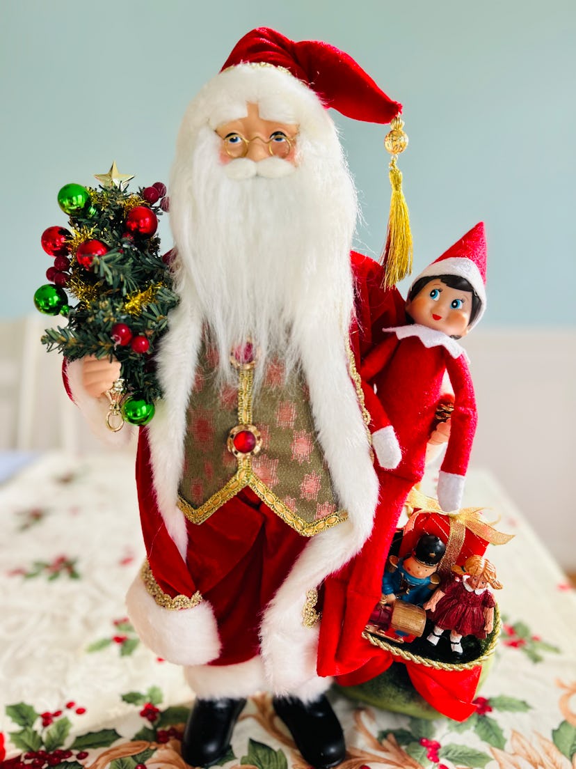 elf on the shelf sitting with a statue of Santa Claus 