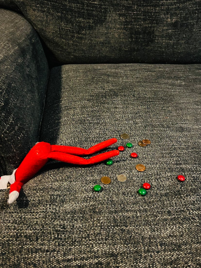 elf on the shelf cleaning the couch surrounded by coins and red & green m&ms