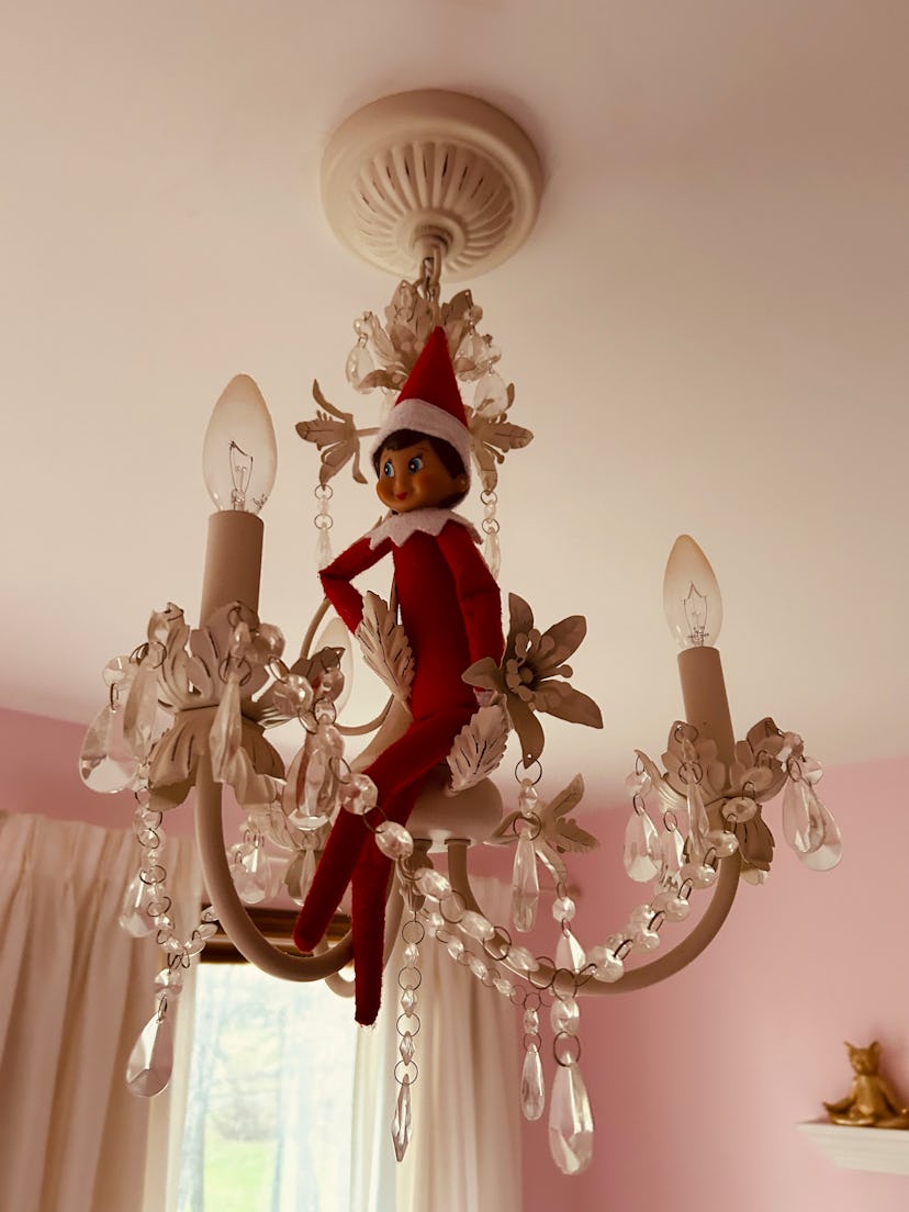 elf on the shelf sitting on top of a chandelier
