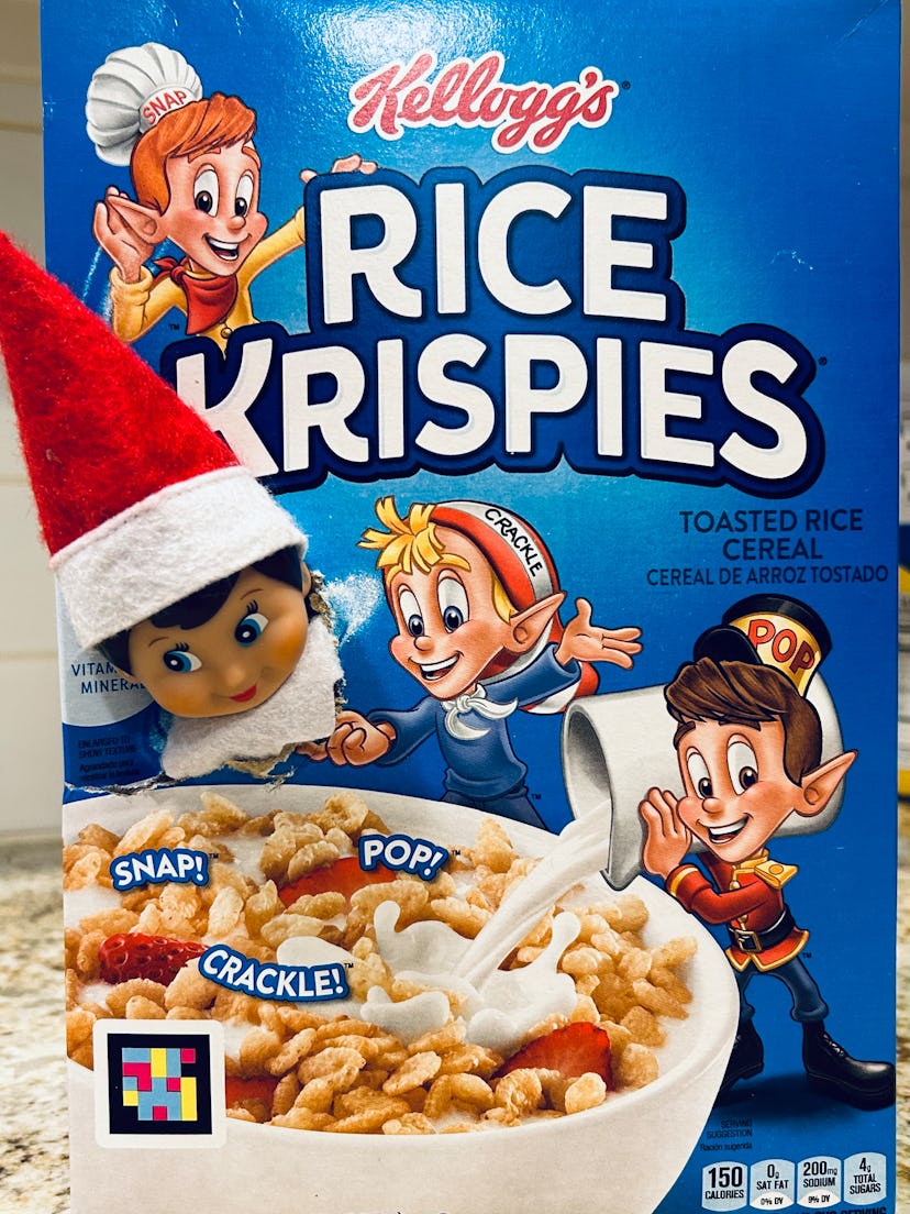 elf on the shelf with its head poking through a Rice Krispies cereal box so it looks like it's hangi...