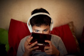 A child with headphones on playing video games on a portable device.