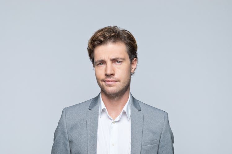 Middle-aged man with light brown hair in grey suit jacket looking at camera suspiciously