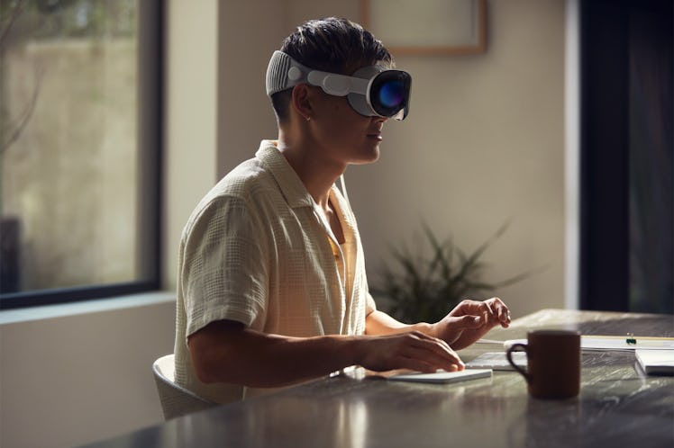 A person wearing an Apple Vision Pro spatial computer headset with they eyes (EyeSight) visible on t...