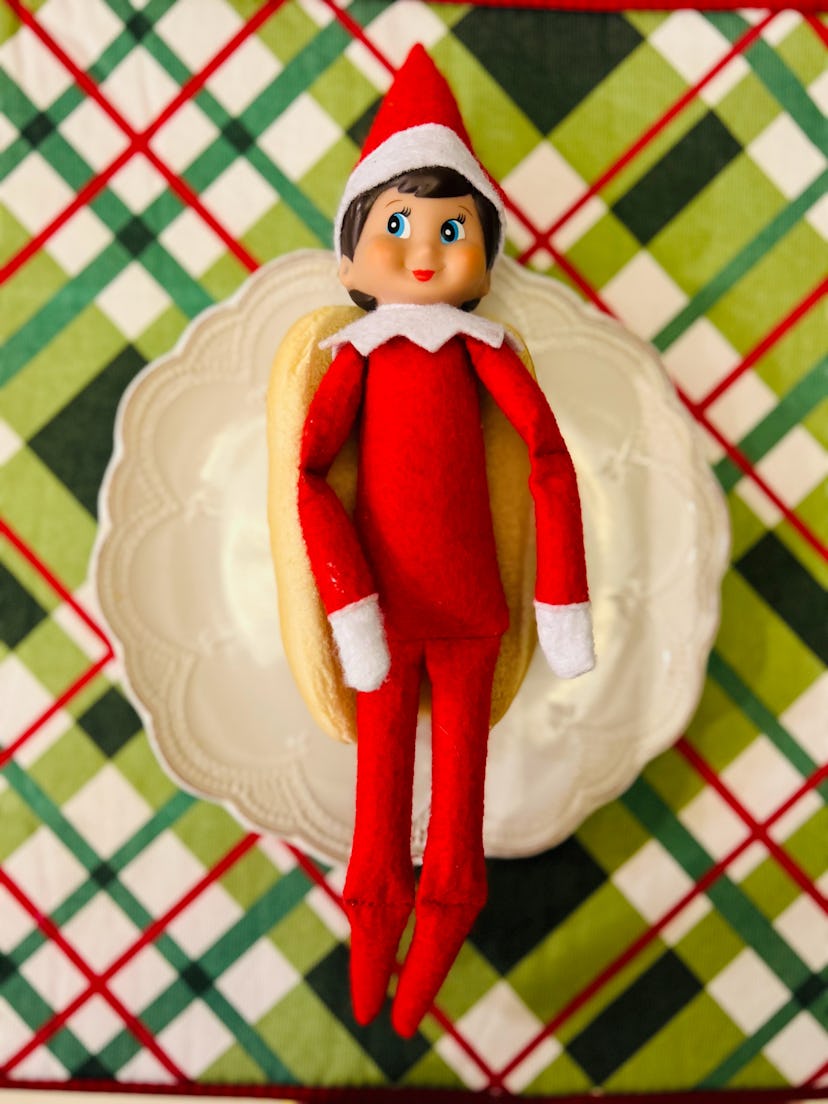 elf on the shelf lying in a hot dog bun