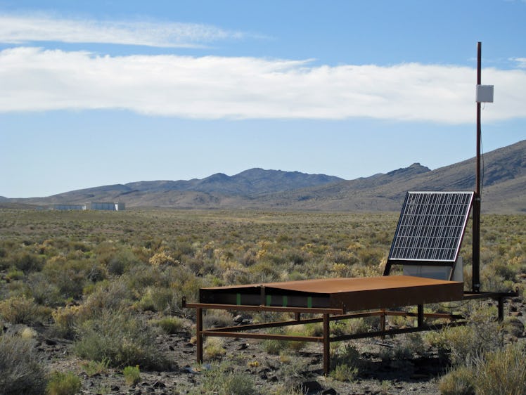 image of a solar panel and a wooden case on table legs in the middle of the desert scrub