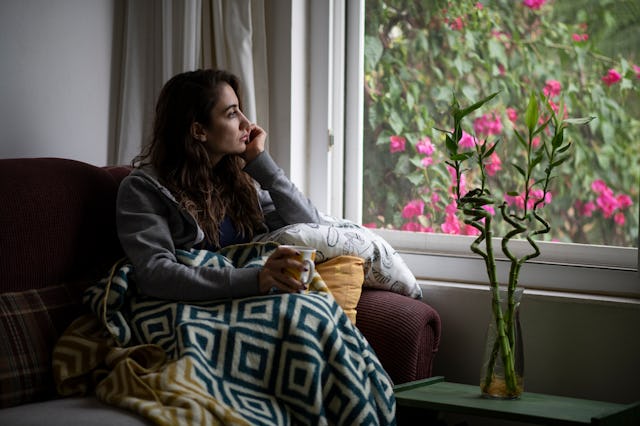 A woman sits alone in her living room, looking out of the window and reflecting.