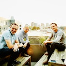 Three middled aged men who are friends sitting on a rooftop and having a conversation in the afterno...