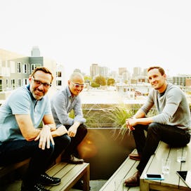 Three middled aged men who are friends sitting on a rooftop and having a conversation in the afterno...