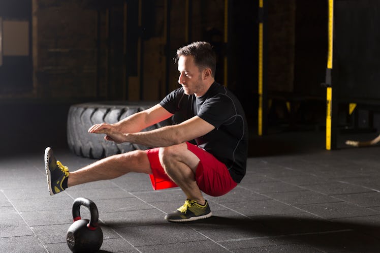 A man doing a pistol squat in a gym.