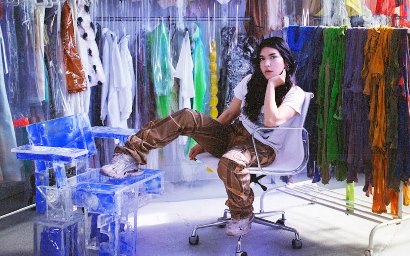 Artist Donna Huanca sits in a chair surrounded by racks of clothing