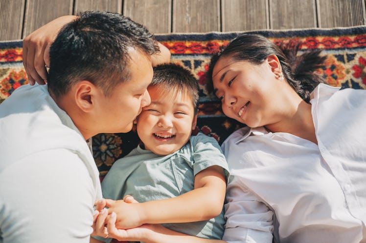 A dad, mom, and their child lie on a rug on the floor together, smiling.