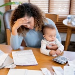 A stressed-out woman looks at her bills and holds her baby.