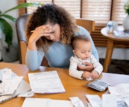 A stressed-out woman looks at her bills and holds her baby.