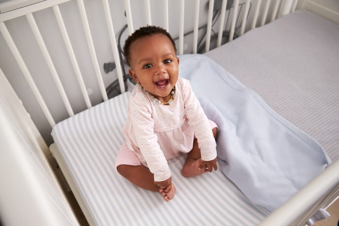 Baby sits in crib smiling and squealing, in a story answering the question "why does my baby shriek ...