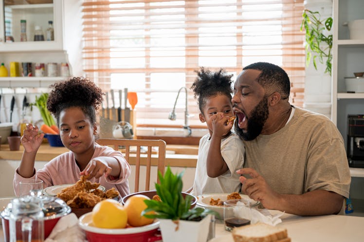 A dad's child puts a piece a food in his mouth as they eat family dinner together at home.