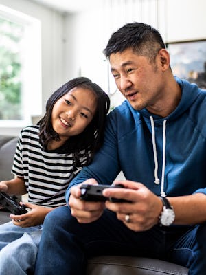 A dad and daughter play video games together on the couch.