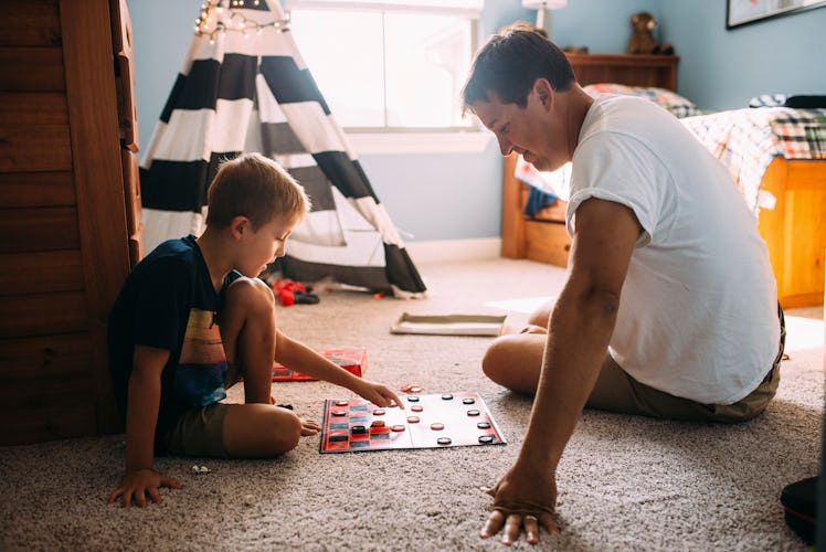 A son and father play checkers on the floor of the boy's bedroom.