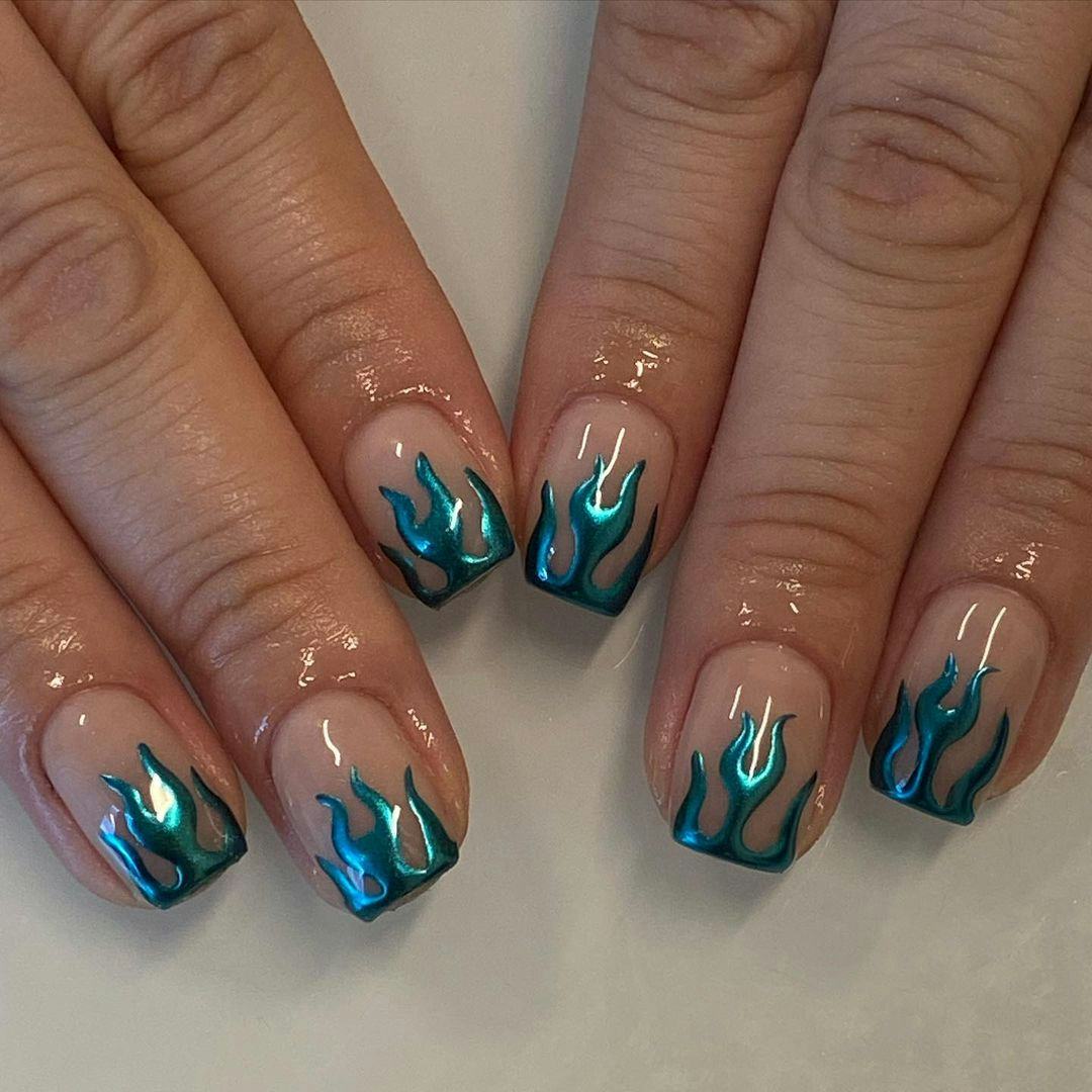 A blue chrome nail design with flame nail art is a popular manicure trend for 2023.