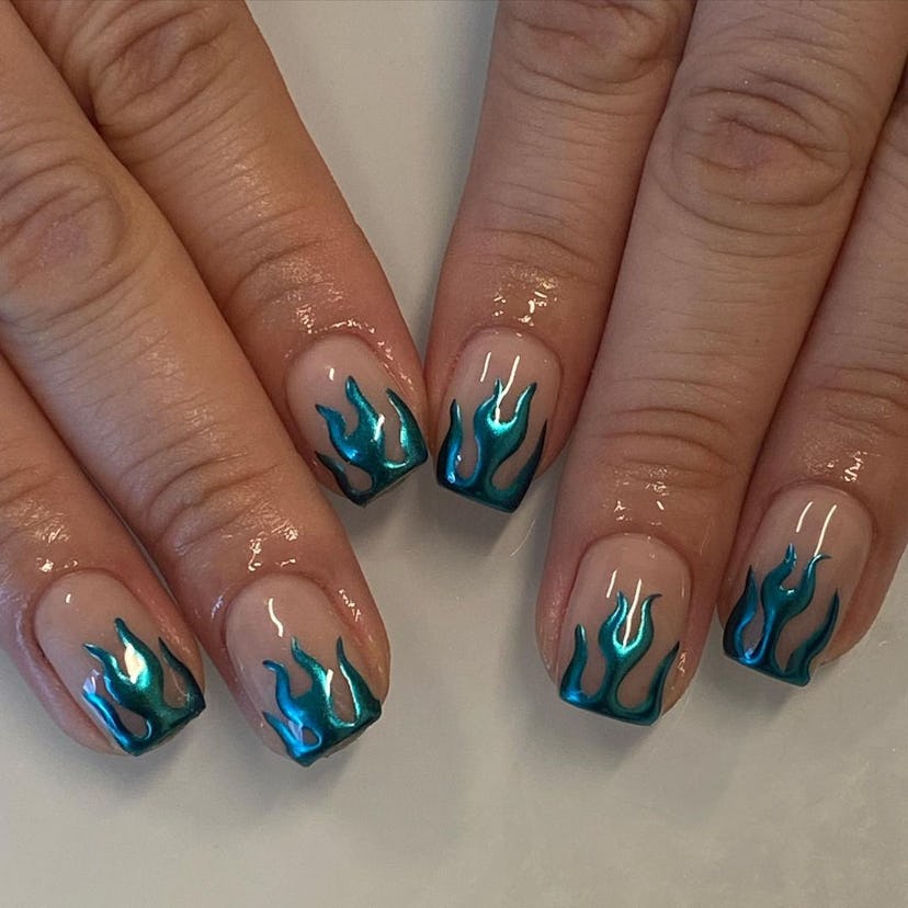 A blue chrome nail design with flame nail art is a popular manicure trend for 2023.