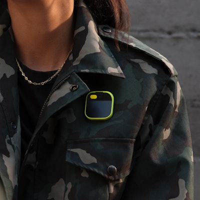 The Ai Pin with a yellow "shield" pinned to a camo jacket.