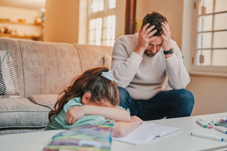 A frustrated father holds his head in his hands as his daughter cries, burying her head in her arms.